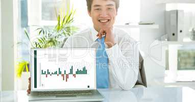 Portrait of businessman with graph on laptop at desk in office