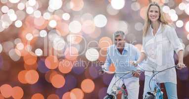 Smiling couple riding bicycles over bokeh