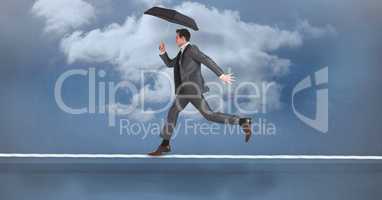 Businessman with umbrella running on rope against sky