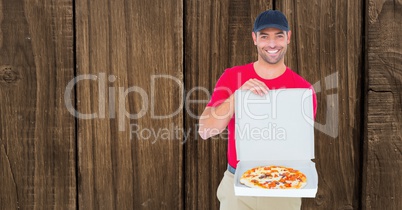 Smiling delivery man showing pizza against wooden wall