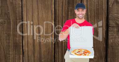 Smiling delivery man showing pizza against wooden wall