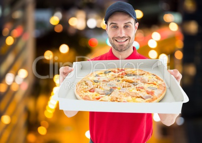Happy deliveryman showing the pizza in the city at night. Lights