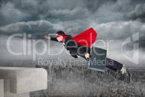Digital composite image of businesswoman wearing cape flying against city