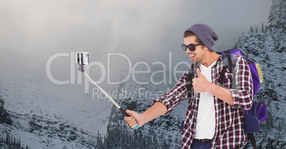 Happy man taking selfie on smart phone against snow covered mountain
