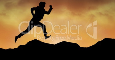 Silhouette business person running over mountains against orange sky