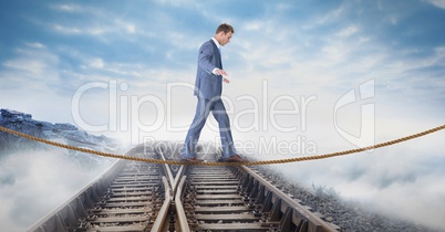 Digital composite image of businessman walking on rope over railway tracks