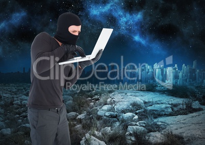 Criminal Man in balaclava on laptop in front of landscape at night