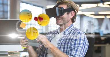 Happy businessman using VR glasses and tablet PC while emojis flying around
