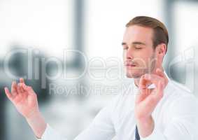 Business man meditating in blurry grey office