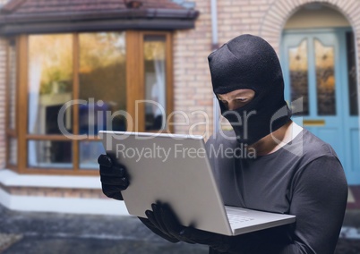 Criminal in hood on laptop in front of home house