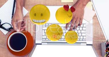 Digital composite image of emojis flying over hands using laptop at table