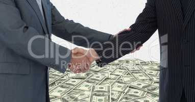 Midsection of businessmen shaking hands with money in background