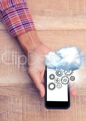 Overhead of hand with phone showing cloud and cog graphics with flare