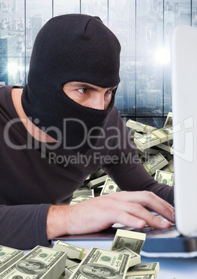 Criminal in balaclava with laptop and money in front of window