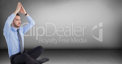 Business man meditating with hand over head in grey room