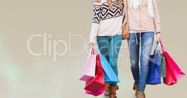 Midsection of female friends with shopping bags standing against beige background