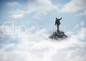 Business man losing balance on mountain peak in the clouds