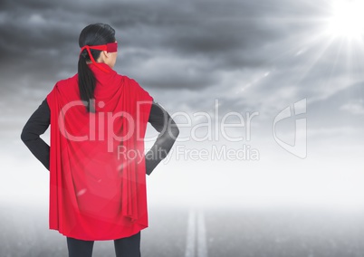 Back of business woman superhero with hands on hips against road and stormy sky with flare
