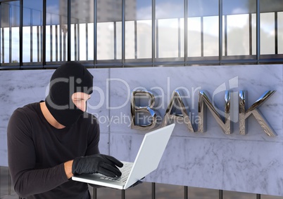 Criminal in hood on laptop in front of bank