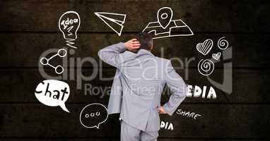 Digital composite image of confused businessman looking at various icons against wooden wall