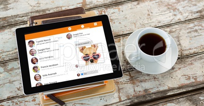 High angle view of chat list in tablet computer on books by coffee cup at table