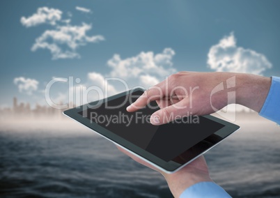 Hands with tablet against blurry skyline and water