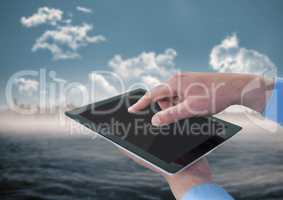 Hands with tablet against blurry skyline and water