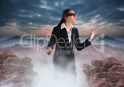 Business woman blindfolded walking on misty mountain peak
