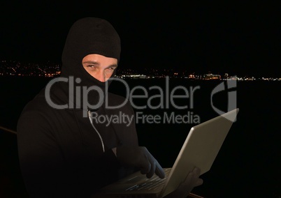 Criminal in hood on laptop in front of night lights