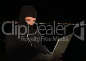 Criminal in hood on laptop in front of night lights