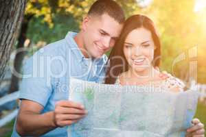 Happy Mixed Race Couple Looking Over A Map Outside Together.