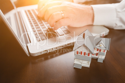 Miniature House Resting on Desktop And Man Using Laptop Computer