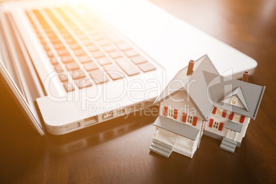 Miniature House And Laptop Computer Resting on Desktop.