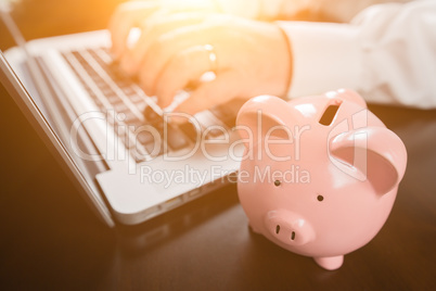 Piggy Bank Near Male Hands Typing on Laptop Computer.