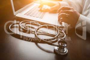 Medical Stethoscope Resting on Desk As Male Hands Type on Comput