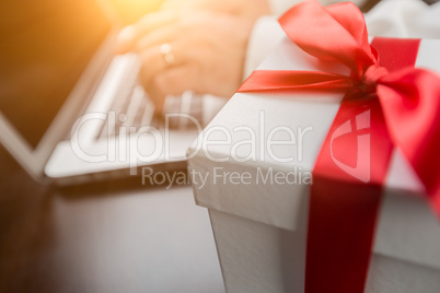 White Gift Box with Red Ribbon and Bow Near Man Typing on Laptop