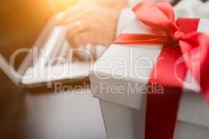 White Gift Box with Red Ribbon and Bow Near Man Typing on Laptop