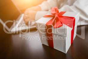 White Gift Box with Red Ribbon and Bow Near Man Typing on Laptop