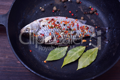 Carp with spices in a black cast-iron frying pan,