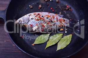 Carp with spices in a black cast-iron frying pan,