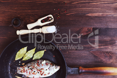 River fish carp with spices in a black cast-iron frying pan
