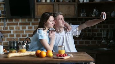 Happy couple taking selfie with phone in kitchen