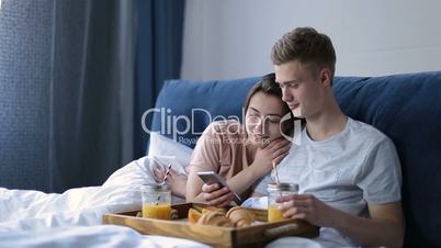 Cheerful couple enjoying romantic breakfast in bed