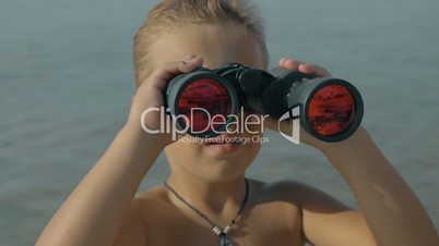 Slow motion view of small boy watching with binoculars against blurred sea