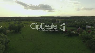 View of forest, lake and country houses against blue sky with sun and clouds in sunset at summer, Russia