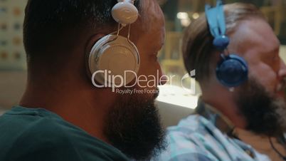 Close up view of two bearded men listening musics using colorful on-ear headset