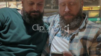 Close up view of two white mature bearded men using smartphone together
