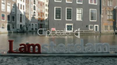 View of small plastic figure of Iamsterdam letters sculpture on the bridge against blurred cityscape, Amsterdam, Netherlands