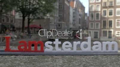 View of small plastic figure of Iamsterdam letters sculpture on the bridge against blurred cityscape, Amsterdam, Netherlands