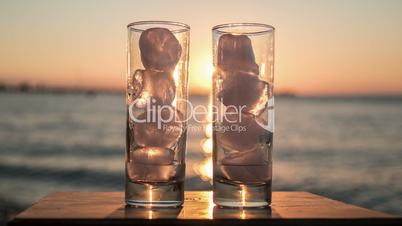 Glasses with melting ice against sea and sunset background